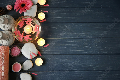 Beautiful spa composition of flower petals with water in bowl and candles on wooden background