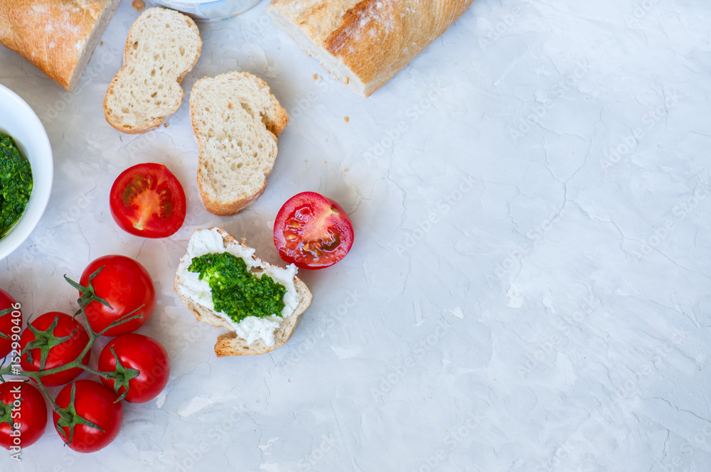 Set of ingredients for bruschettas with goat cheese, pesto sauce and tomatoes abd baguettes on a white stone background. Top view and copy space. Set of ingredients for bruschettas with goat cheese, pesto sauce and tomatoes abd baguettes on a white stone background. Top view and copy space.