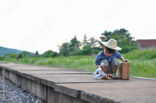 Happy boy with hat suitcase and toy on railway station wait a train