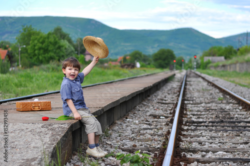 Boy on the railway station with a suitcase raised his hat in the air