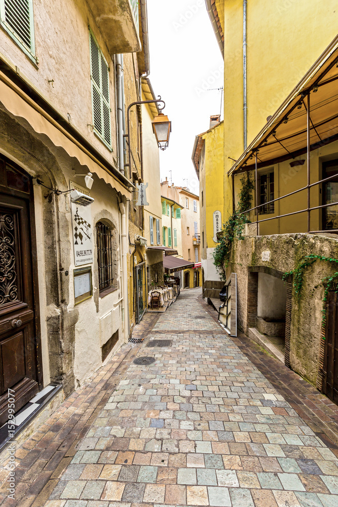 Narrow pedestrian street in Old Town of Cannes, France with sidewalk cafes, souvenir shops.
