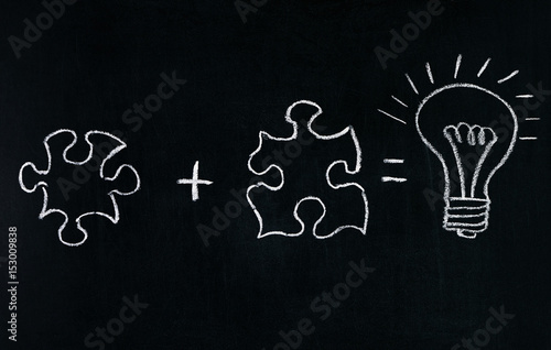 Businessmans Hand drawing puzzle on blackboard to explain business concept. Solving puzzle together. Drawing light bulb on blackboard. Combining the wisdom for developing new idea.