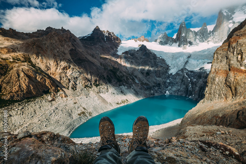 Tracking boots shoes on a blue lake background among mountains and cloudy sky