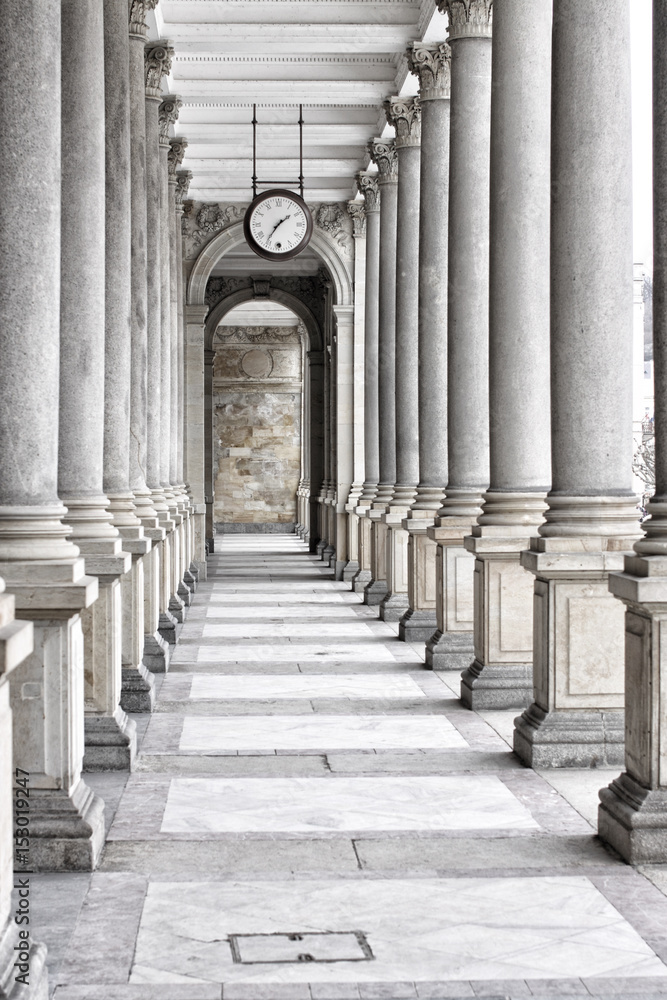 Fototapeta premium Colonnade of tall columns with clock by the ceiling