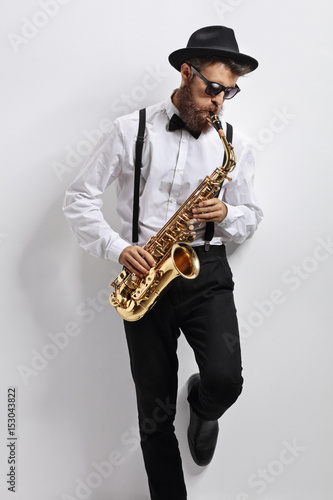 Jazz musician leaning against a wall and playing saxophone