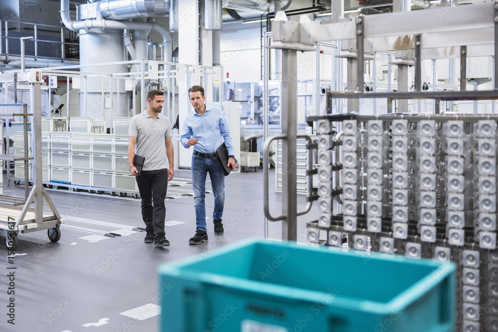 Two men walking and talking in factory shop floor Two men walking and talking in factory shop floor