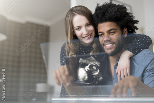 Smiling couple looking at ultra sound picture of baby on futuristic screen photo