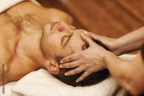 Handsome young man enjoying massage at spa center