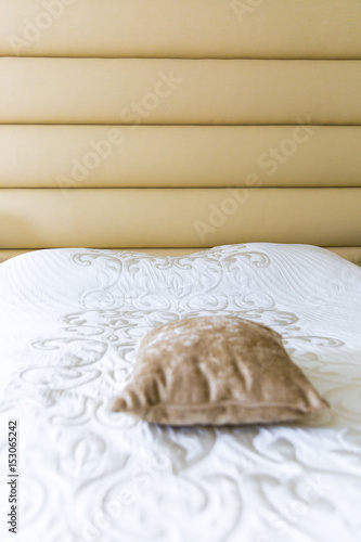 close up on a bed with beige padded headboard and matching cushion and white bedspread