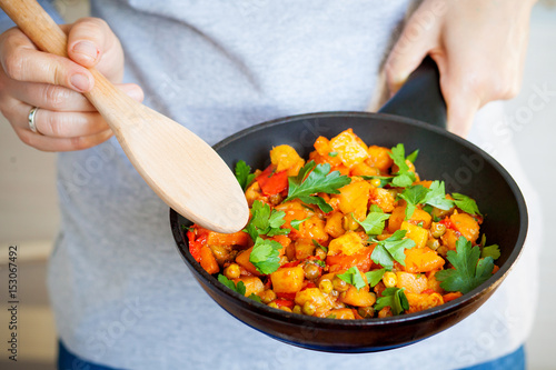 Woman holds a frying pan with vegetable stew and stir wood spoon. Healthy eating.