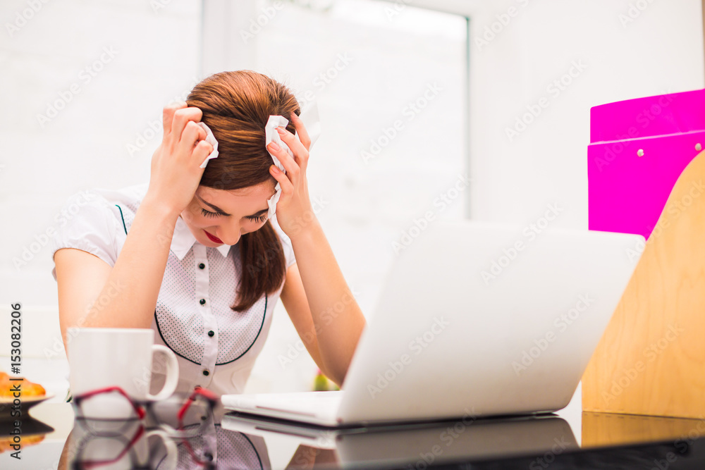 Portrait of young sick office worker who sits at the table at the office, keeps napkins in hands and has headache Portrait of young sick office worker who sits at the table at the office, keeps napkins in hands and has headache