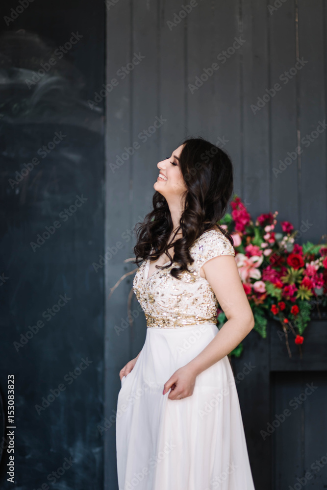 beautiful brunette girl in white wedding dress laughing with eyes closed,emotions with a smile is, sweeping the Studio, grey background, decoration with red flowers