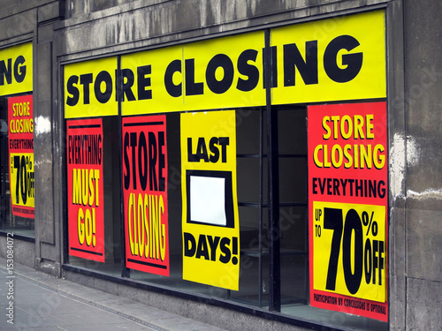 Large printed signs in a department store window announcing store closing and price reductions.