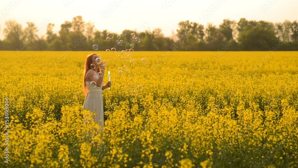 Young beautiful red-haired woman puffing bubbles in a flowering field Young beautiful red-haired woman puffing bubbles in a flowering field