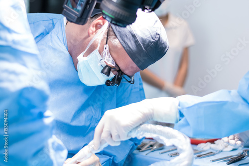 A male dentist in uniform perform dental implantation operation on a patient at dentistry office.