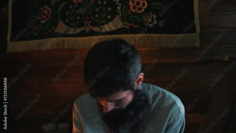 Bearded caucasian man in traditional russian kosovorotka shirt sitting in wooden house talking with monk Bearded caucasian man in traditional russian kosovorotka shirt sitting in wooden house talking with monk