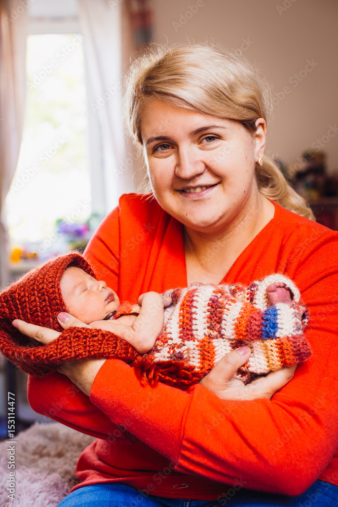 Pretty blonde woman in orange sweater holds little baby on her arms Pretty blonde woman in orange sweater holds little baby on her arms
