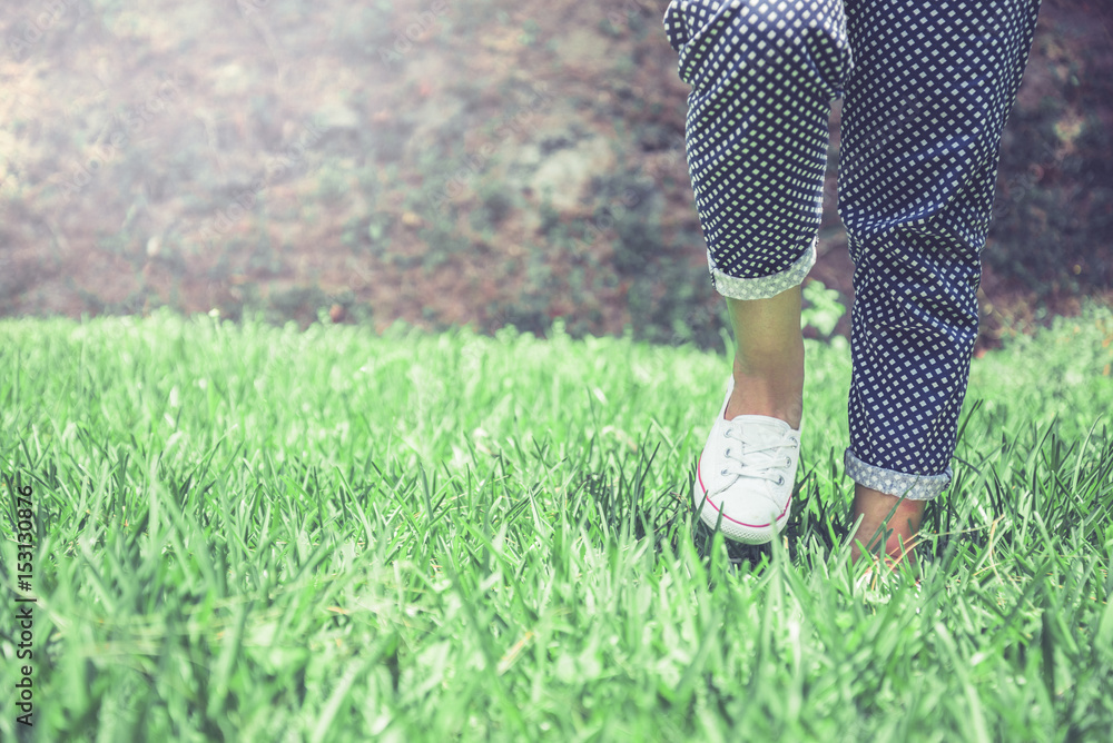 Legs of women walking on a green meadow.