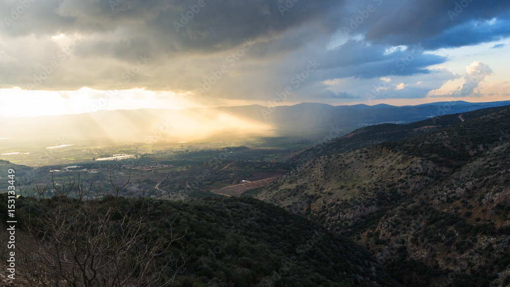 Magnificent landscape of the Golan Heights, the rays of the setting sun make their way through heavy clouds and dispersing the darkness above the valley