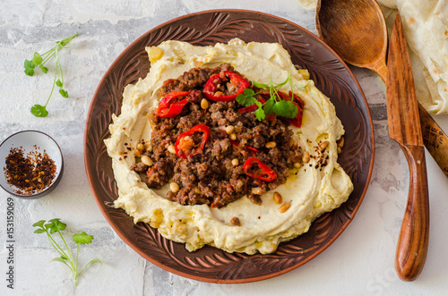 Creamy hummus with spicy mutton minced meat in clay bowl on stone background. Ramadan food. Top view