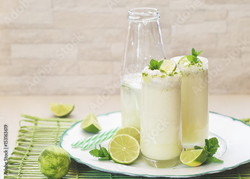 Delicious Brazilian lemonade or limeade in retro bottle and glasses,  decorated with lime slices and mint . Macro, selective focus, blank space