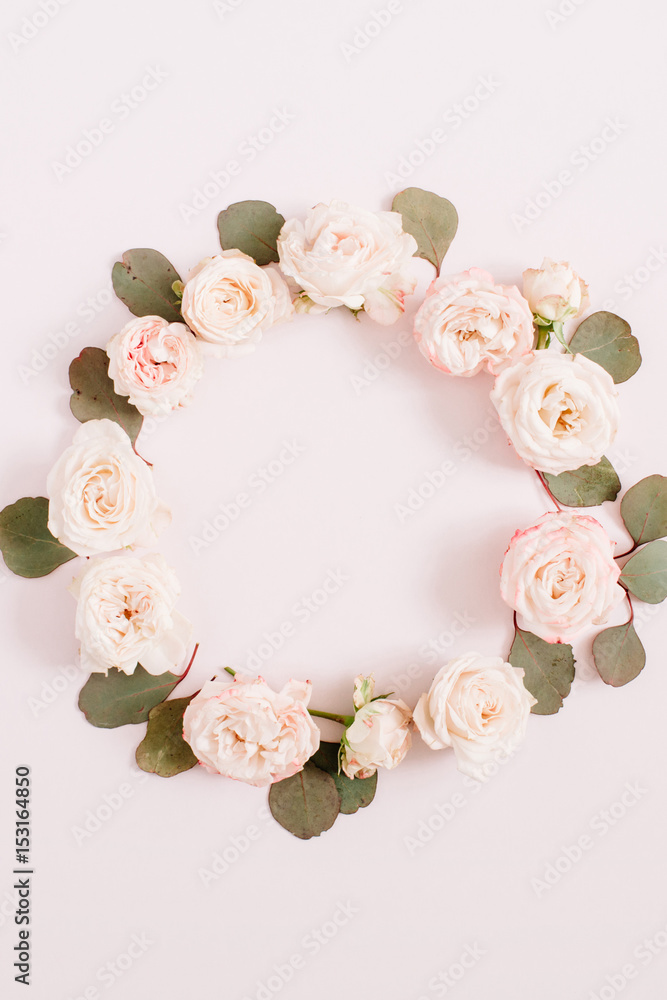 Flower frame made of beige roses, eucalyptus branches on pale pastel pink background. Flat lay, top view. Floral texture background.