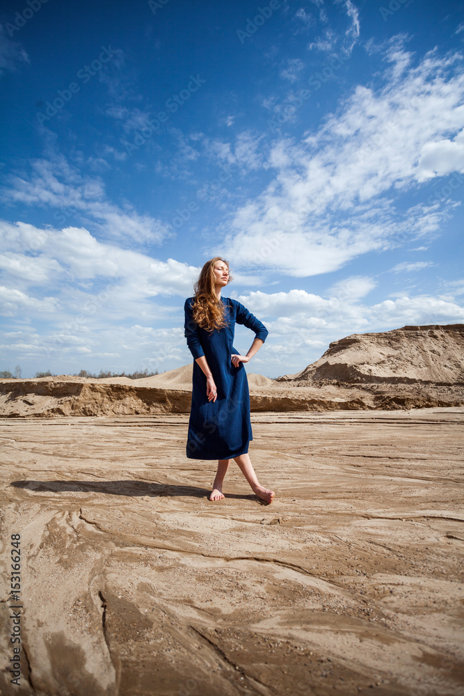girl in blue dress among sand mountains in desert.