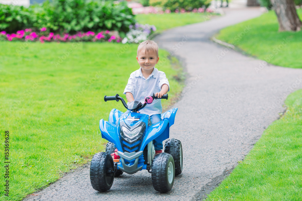 Portrait of smiling little Caucasian boy toddler driving blue electric car on the road path outside on spring summer day, seasonal child activity concept, healthy childhood lifestyle Portrait of smiling little Caucasian boy toddler driving blue electric car on the road path outside on spring summer day, seasonal child activity concept, healthy childhood lifestyle