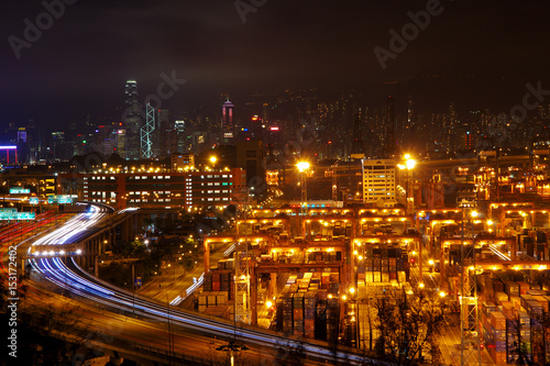 Aerial view of the Kwai Tsing Container Terminals in Hong Kong with light trail from vehicles and skyscrapers as background