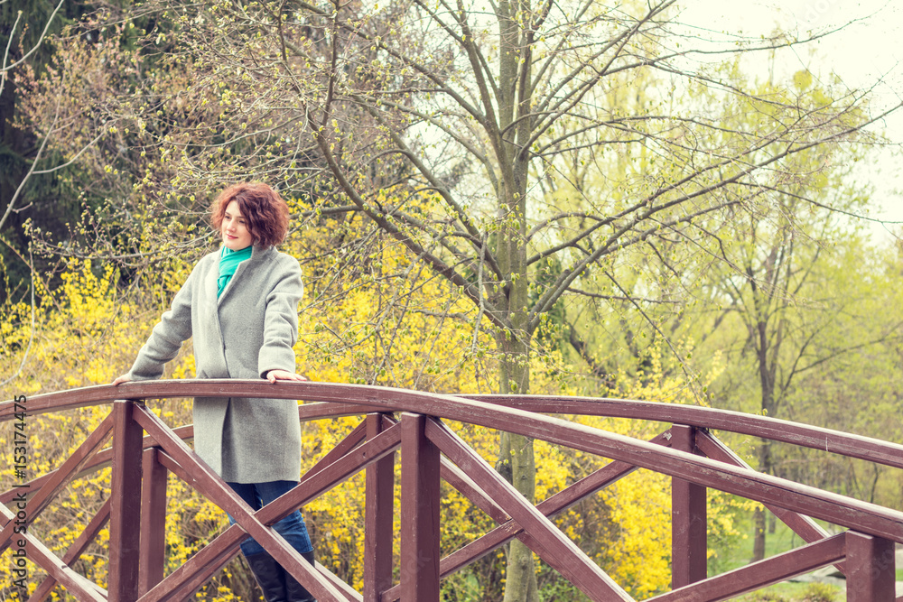 Pretty young red head woman on the bridge in spring park. Green trees and forsythia blossoms background. Pretty young red head woman on the bridge in spring park. Green trees and forsythia blossoms background.