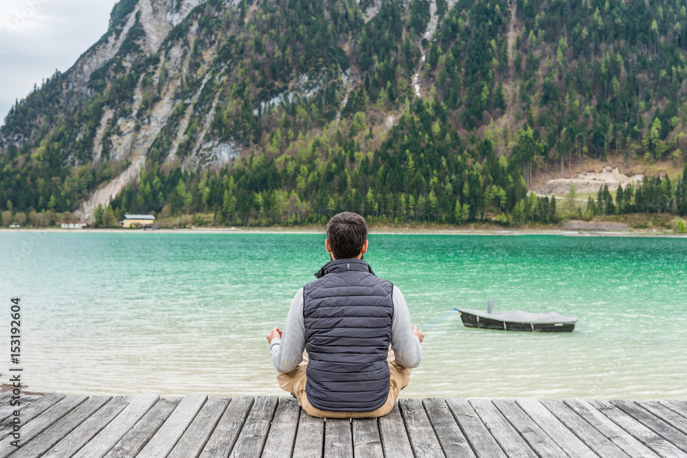 Man sitting on a lake wooden pier making yoga and meditation. Health sport relaxation concept