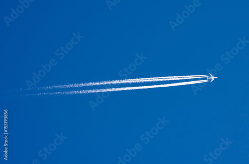 Large passenger liner and trail from an airplane in a blue sky.