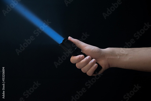 Black flashlight a beam of light directed at the top in male's hand isolated from right side of the frame on black background