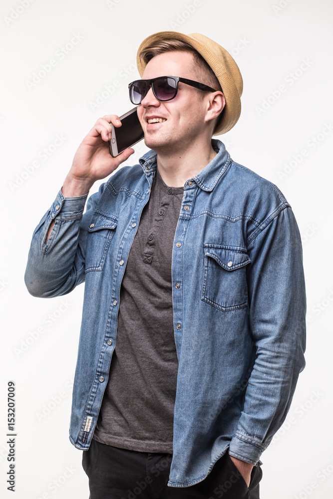 Cheerful young man in hat and sunglasses standing and talking on mobile phone over white background Cheerful young man in hat and sunglasses standing and talking on mobile phone over white background