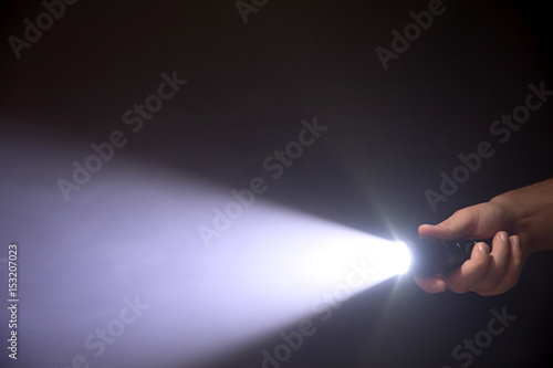 Black flashlight a beam of light directed at the viewer in male's hand isolated from right side of the frame on black background photo