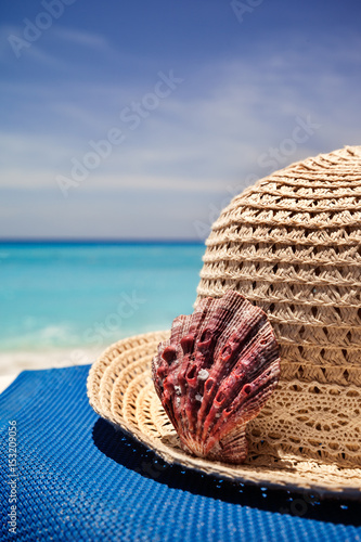 Straw hat with red shell on a tropical beach, vacation concept