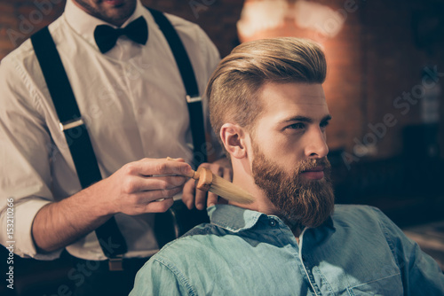 Classy dressed barber shop hairdresser is cleaning client`s neck with a brush and presents his work for him. Stunning! Hairdo looks trendy and so perfect