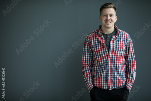 Handsome young man in smart casual wear looking at camera and holding hands in pockets while standing against grey background