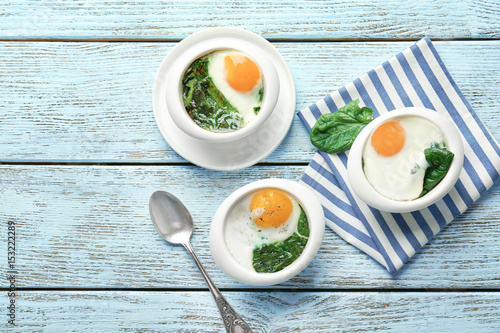 Obraz na plátně Bowls with tasty eggs and spinach on wooden table