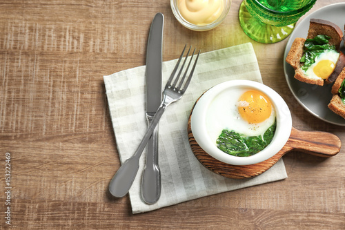 Bowl with tasty egg and spinach on wooden table