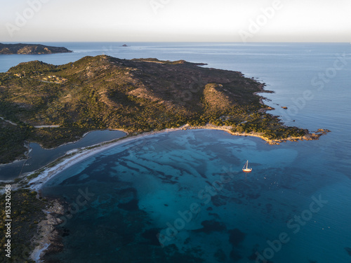Aerial view of a sailboat in a bay of the Emerald coast at sunset in Sardinia, Italy.