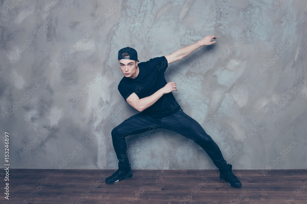 Portrait of a young handsome dancer making his moves. Guy is wearing black t shirt and jeans and cap