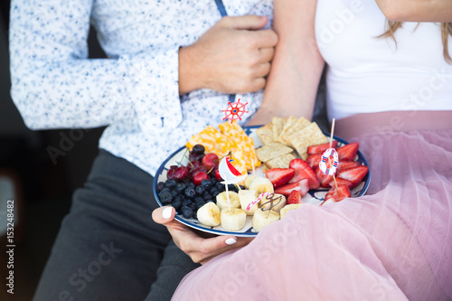 Plate with fruit and snack. Cheese, cracers, cherry, strawberry, blueberry, banana, snakcs. Nautical toothpicks. Plate on the couple hand, hands