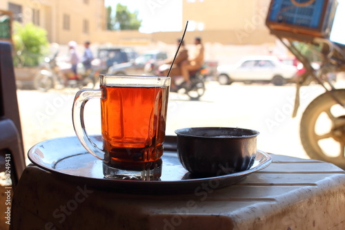 Detail of a bedouin cup of tea with bikes and people in the streets on soft background, Bahariya Oasis, Egypt