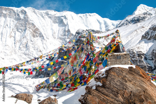 Buddyjskie flagi modlitewne w Annapurna Base Camp i ośnieżone góry w tle. 
