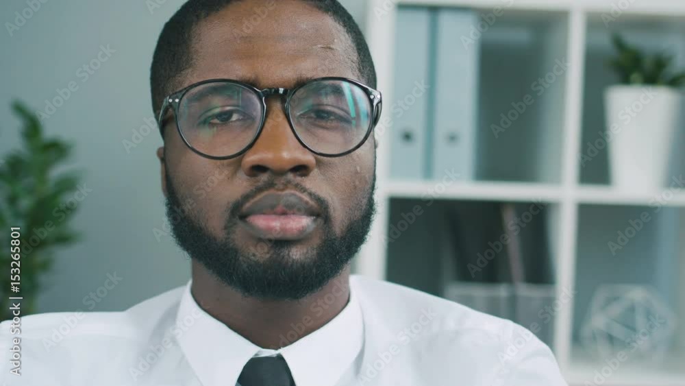 Close up portrait of young african business man looking stright on camera, posing and smiling on camera in the office background. Close up portrait of young african business man looking stright on camera, posing and smiling on camera in the office background.