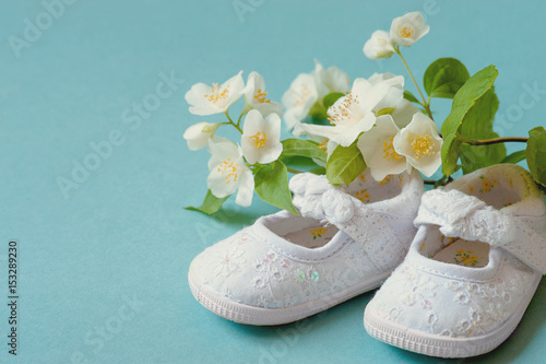 Cute, White Vintage Leather Infant Baby Shoes with spring flowers on Cyan Background and room or space for copy, text, your words. Concept of a newborn, christening