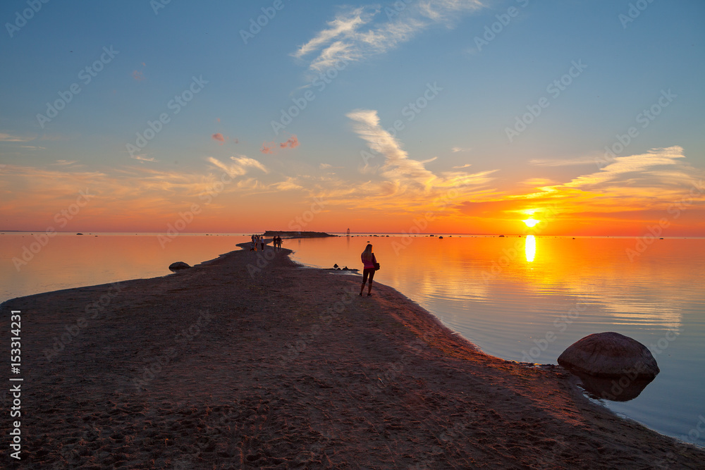 Colorful sunset over sand coast of the sea. Woman enjoying dawn