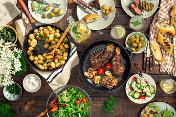 Dinner table with meat grill, roast new potatoes, different food