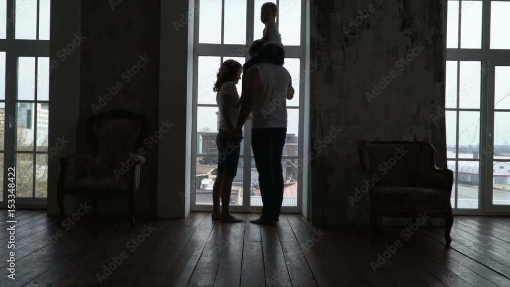 The young couple is by the window of the apartment. The young family approaches a window of the apartment. Siluyet of a young family at a window. Silhouette at the window. The young couple is by the window of the apartment. The young family approaches a window of the apartment. Siluyet of a young family at a window. Silhouette at the window.
